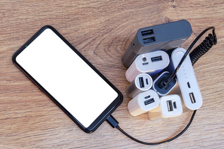 Set of power banks with a telephone on a wooden table. A portable charger charges a smartphone with...