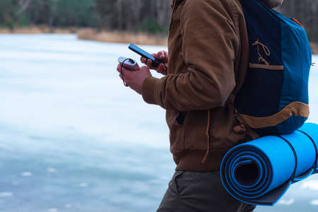 Tourist with a backpack holds a smartphone in his hands and charges it from a power bank. A traveler...