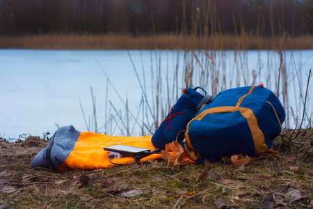 Smartphone is charged using a portable charger. Power Bank charges the phone outdoors with a backpack for tourism in the background of nature and the riverの写真素材