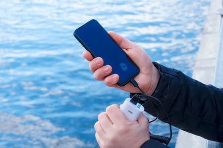 A man charges a smartphone with a power bank. The phone in hand is being charged with a portable...