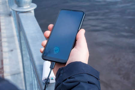 A man charges a smartphone with a power bank. The phone in hand is being charged with a portable...