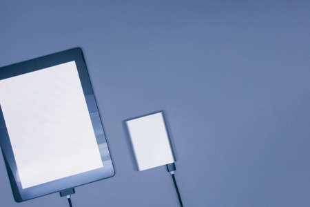 Portable charger charges a mockup Tablet with white screen isolated on a gray background.