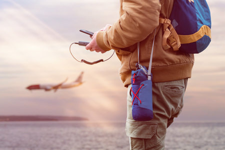 Tourist holds a power bank in his hands and charges a smartphone while traveling. A man on the background of the sea and the plane on vacationの写真素材