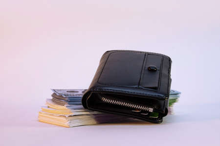A large bundle of dollars and euros with a wallet on a light background