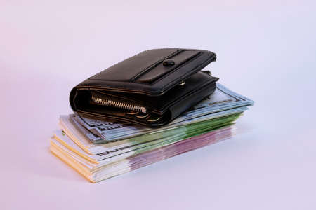 A large bundle of dollars and euros with a wallet on a light background