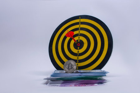 Concept of success and goal achievement. Round dart board with a bundle of dollars, euros and a Bitcoin coinの写真素材