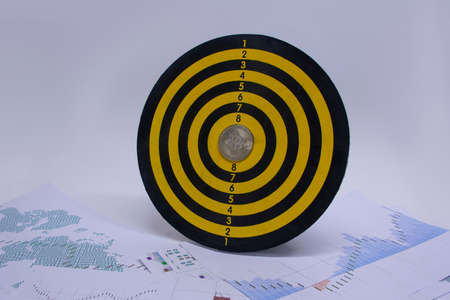 Concept of success and goal achievement. Round dart board with a bitcoin coin in the center of the circle on the background of graphs and diagrams on paperの写真素材