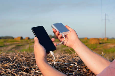 Power Bank charges your phone while traveling. A man holds a smartphone and a portable charger in...