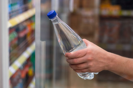 Man holds in his hand a plastic bottle with pure mineral water on the background of a shop windowの写真素材