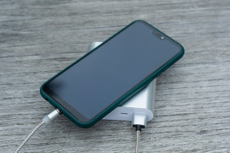 Power Bank charges a smartphone on a wooden bench in the parkの写真素材
