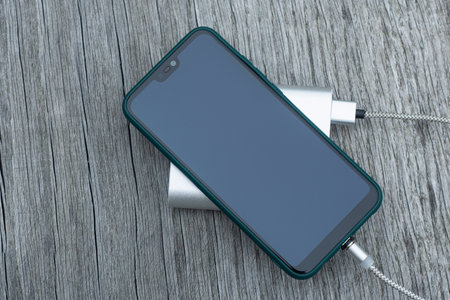 Power Bank charges a smartphone on a wooden bench in the parkの写真素材