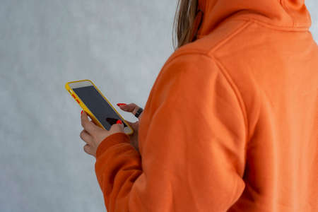 A girl in an orange sweater holds a smartphone in her hands.の写真素材
