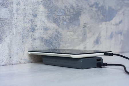 Tablet charging with power bank on a gray wooden table. Portable charger for charging devicesの写真素材