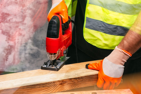 Male worker holds a close-up jigsaw electric in his hands against the background of a concrete wallの写真素材