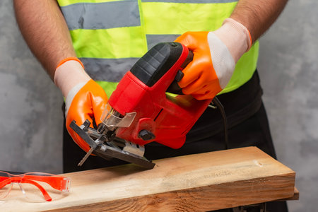 Male worker holds a close-up jigsaw electric in his hands against the background of a concrete wallの写真素材