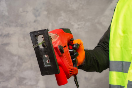 Male worker holds a close-up jigsaw electric in his hands against the background of a concrete wallの写真素材