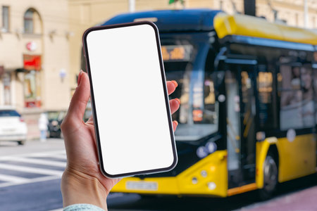 Girl holds a mock-up of a smartphone with a white screen in her hands at a bus stop against the backdrop of a busの写真素材