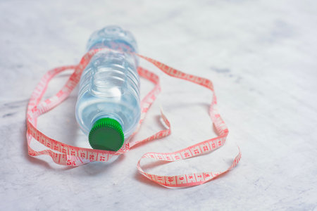 Plastic water bottle isolated on white background with still water and a measuring tape on a light...