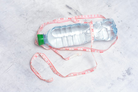Plastic water bottle with still water and a measuring tape on a light background. Concept of losing weight and healthy lifestyleの写真素材