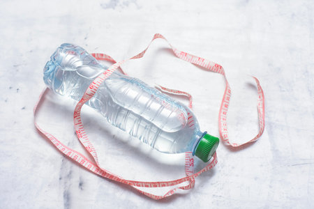 Plastic water bottle isolated on white background with still water and a measuring tape on a light background. Concept of losing weight and healthy lifestyleの写真素材