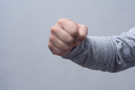 Close-up of a man in a sweater, doing a fist bump against a gray wall.の写真素材
