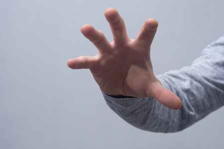 Close-up of a man in a sweater, making a hand grip with open palm against a gray wallの写真素材