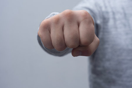 Close-up of a man in a sweater, doing a fist bump against a concrete wall.の写真素材