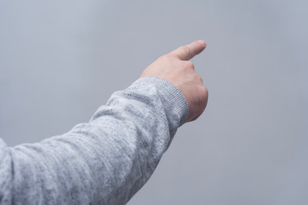 Concept of pointing finger. Close-up of a man in a sweater pointing his finger forward against a gray wallの写真素材