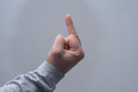 Man in a sweater showing a crude gesture, middle finger sign, close-up against a gray wallの写真素材