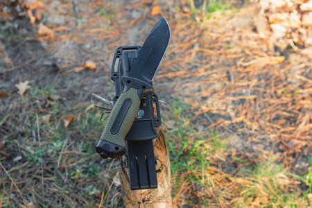 Tactical knife with a green handle in the forest. Tool against the natural leatherの写真素材