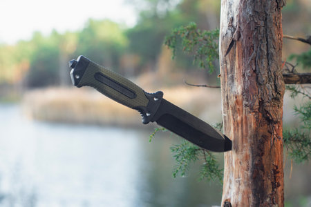 Tactical knife with a green handle in the forest. Tool against the natural leather