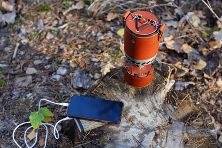 Charge your smartphone while traveling with the Powerbank. The portable charger charges your phone with a camping gas burner in the background.の写真素材