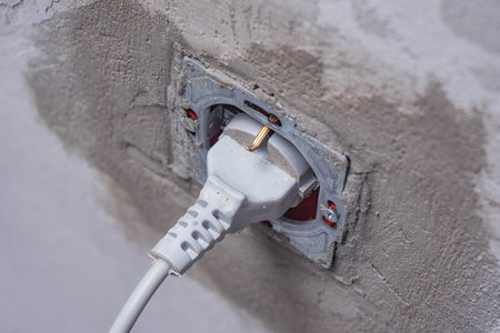 Close-Up of a power plug connected to an electrical socket during renovation. Electrical socket with a plug connected on a dusty wall, representing renovation workの写真素材