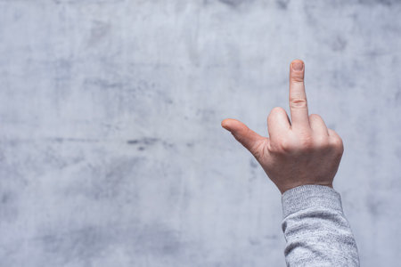Man in a shirt showing a rude gesture, middle finger sign, close-up against a concrete wallの写真素材