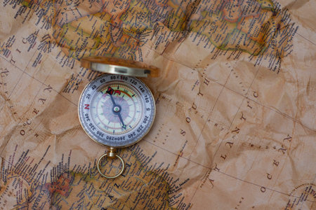 Antique brass compass resting on a world map, symbolizing travel and adventure