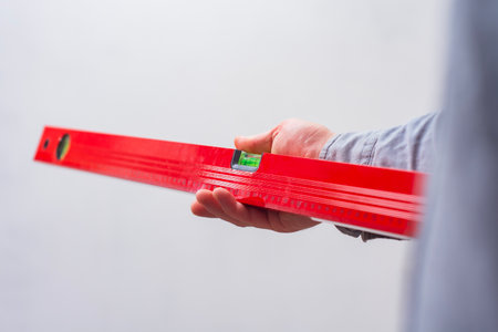 Close-up of a hand holding a red construction level. Tool for DIY, repair, and accuracy