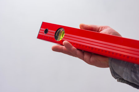 Close-up of a hand holding a red construction level. Tool for DIY, repair, and accuracyの写真素材