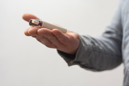 Close-up of a male hand holding a white electronic cigarette with a heated tobacco stick. Photography on a Light Backgroundの写真素材