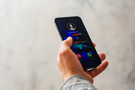 Close-up of a hand holding a smartphone with an incoming call screen. Display shows Incoming call with green accept and red decline buttonsの写真素材