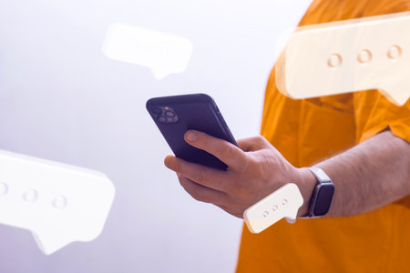 A man in an orange shirt holding a smartphone, surrounded by floating social media chat iconsの写真素材