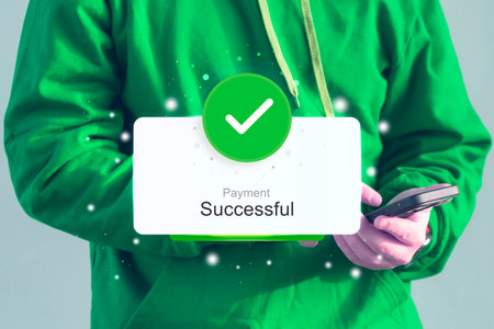 Man wearing a green hoodie holds a smartphone displaying a Payment Successful notification with a...