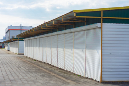 A row of closed market stalls with white shutters with blue sky