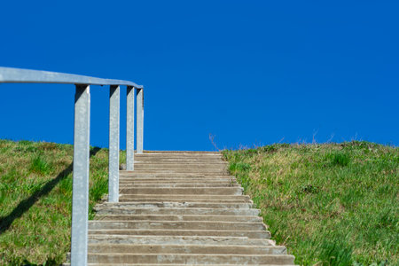 Concrete stairs with railing on grassy hill under blue sky