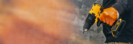 A construction worker in orange gloves holds a power drill against a concrete wall. Concept construction and renovation themesの写真素材