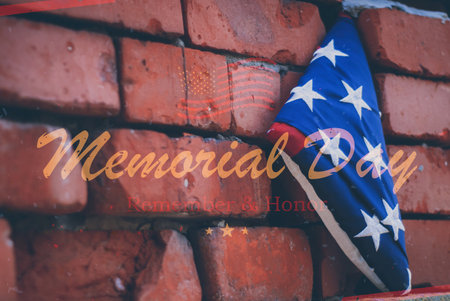 Close-up of a folded American flag on a red brick wall with the words Memorial Day Remembers and Honor. A symbol of remembrance and national prideの写真素材
