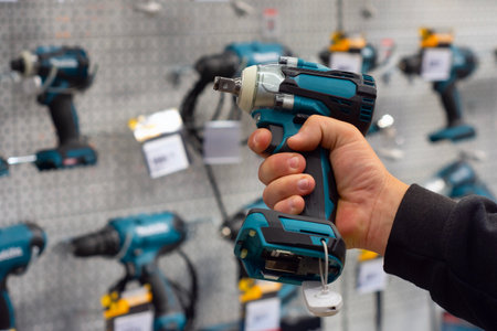 A hand holds a teal power drill in front of a hardware store display with various tools. Concept power tools and construction suppliesの写真素材