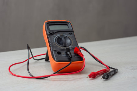 An orange digital multimeter with black and red measuring probes rests on a wooden table. An electronic measuring instrument for checking voltage, current and resistanceの写真素材