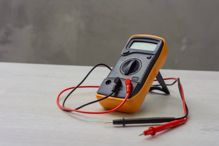 An orange digital multimeter with black and red measuring probes rests on a wooden table. An electronic measuring instrument for checking voltage, current and resistanceの写真素材
