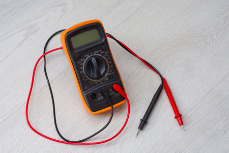 An orange digital multimeter with black and red measuring probes rests on a wooden table. An electronic measuring instrument for checking voltage, current and resistanceの写真素材
