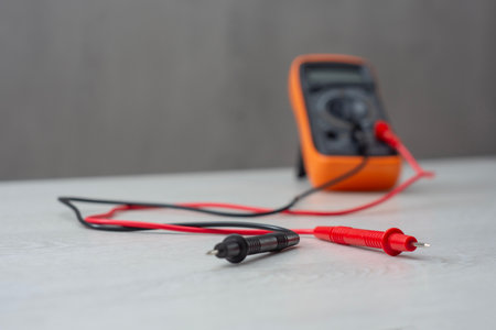 An orange digital multimeter with black and red measuring probes rests on a wooden table. An electronic measuring instrument for checking voltage, current and resistanceの写真素材